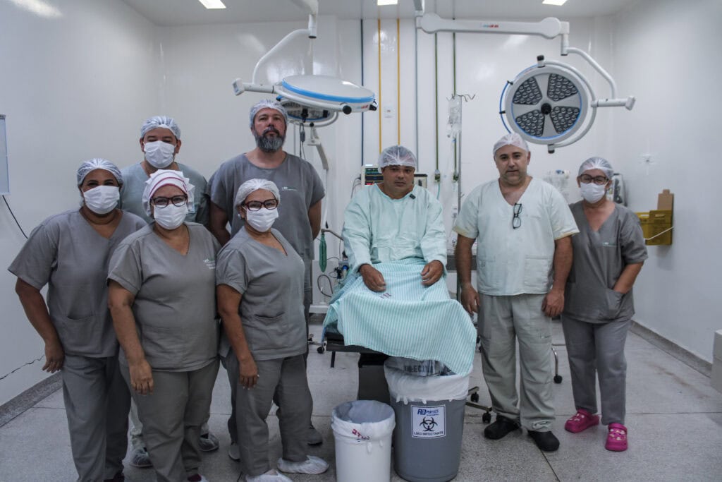 Ao lado do paciente, parte da equipe responsável pelo procedimento: médico ortopedista Demian Miziara, médico anestesista Francisco Lopes, os instrumentadores Luiz Augusto da Silva e Elisete Gonçalves Santos, a enfermeira Ediná Costa e as circulantes Marleide Aires e Lucia Dutra. Foto: Tiago Araújo/Sesacre
